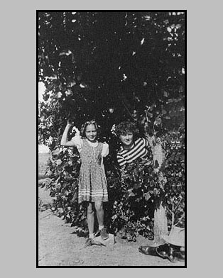 <Adrienne and her first cousin deloris standing by a popular tree behind the ranch house. Notice dad's hat and boots in the lower right hand location of the photo>