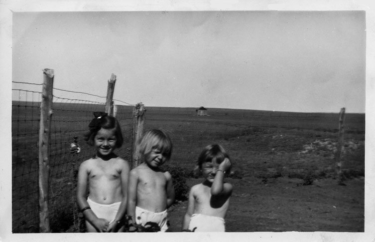 <donna adrienne sheila standing in front yard with little one room school house in the background>