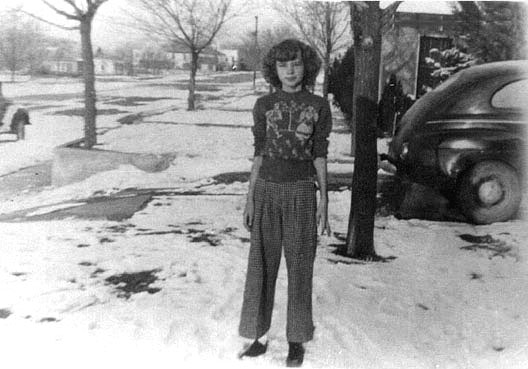 <Adrienne standing in the front yard of the Ft Sumner house wearing a christmas sweater. Snow is on the ground and the 1940 ford can be seen in the background>