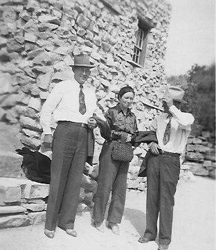 <claud brooks, the husband of johnie's cousin, and adron and johnie standing in front of a rock building>