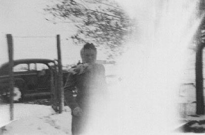<johnie turner standing in snow in ramon ranch yard, black 1940 ford in background front yard gate standing open>