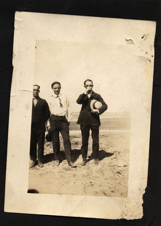 <three men posed for the camera. One man has his hat tuckerd under his arm.>